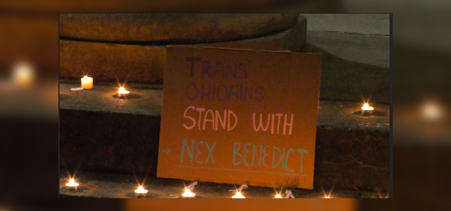 A cardboard sign reads "Trans Ohioans Stand with Nex Benedict." It sits on steps surrounded by candles