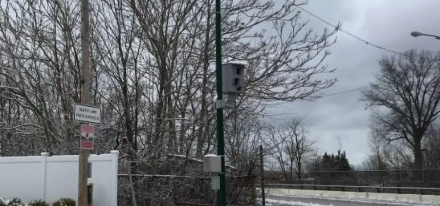 A traffic camera is set up on a utility pole along a street.