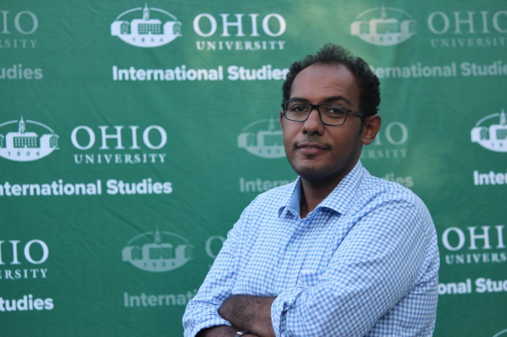 Ahmed Hamed poses for a photo in front of a wall promoting Ohio University International Studies.