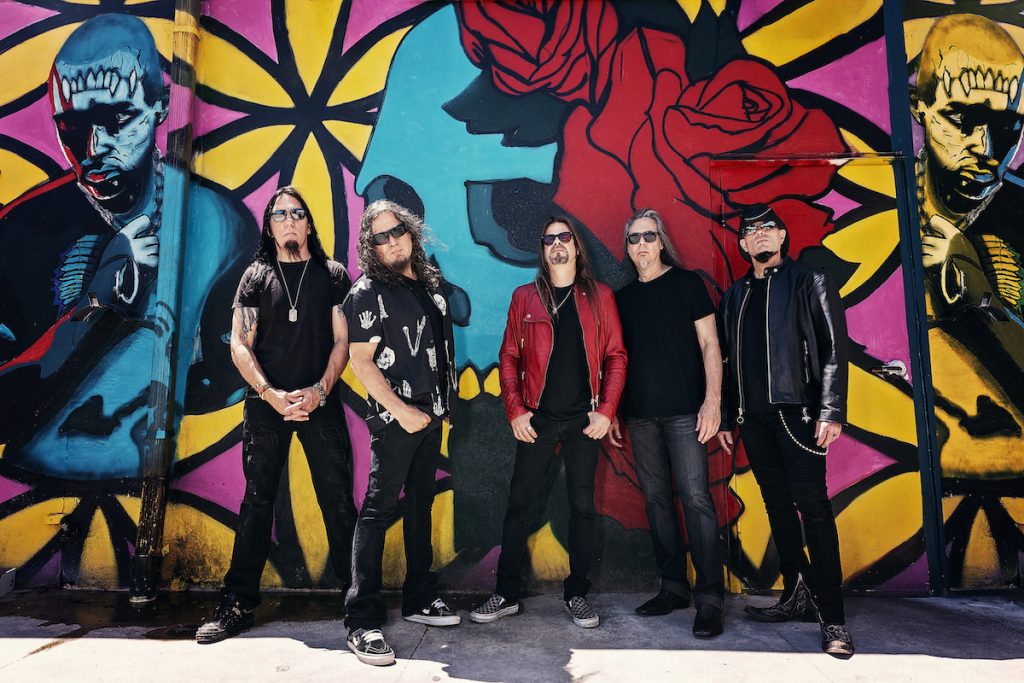 A promotional image of the band Queensryche. They are all posed against a wall of graffiti. 