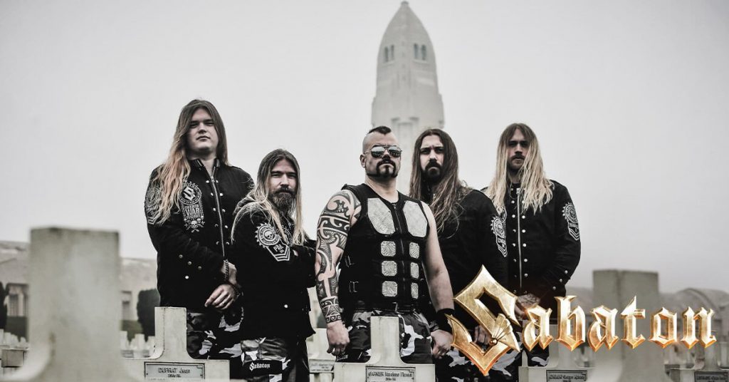 A promotional image of the band Sabaton. All the band members are wearing black and are posed outside against a gray landscape. 