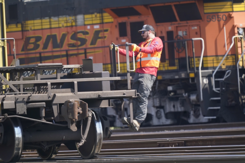 A worker holds himself steady on the handlebars of a rail car.