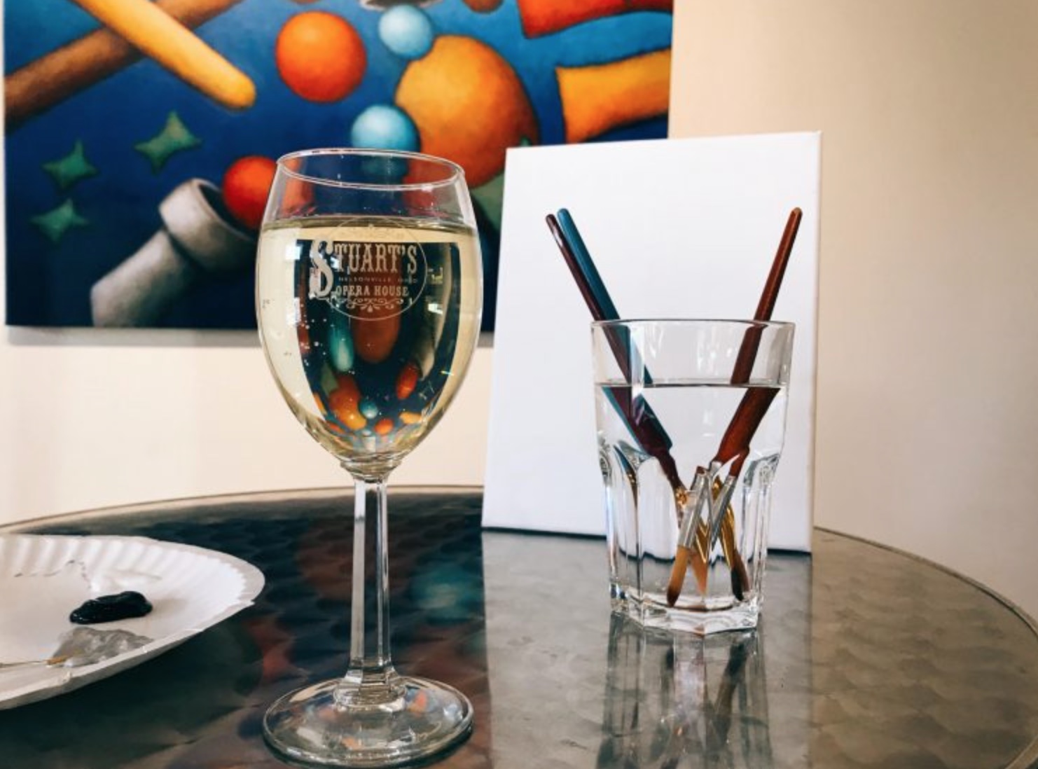 An image of a wine glass next to a glass with paintbrushes