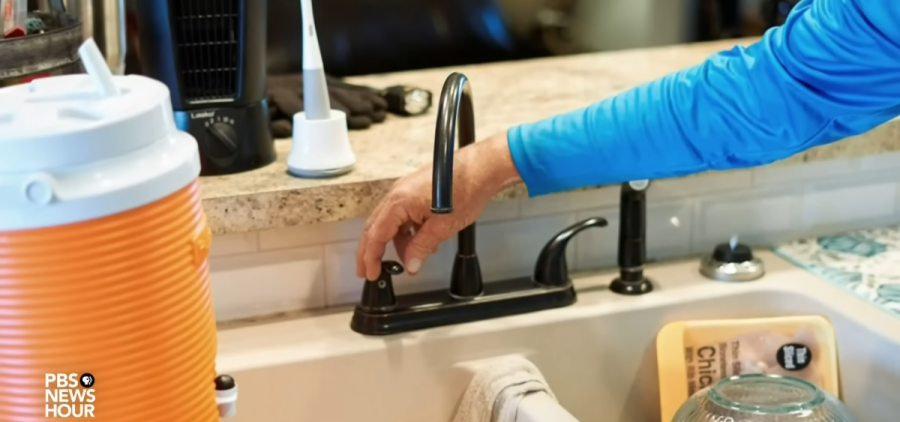 A hand reaches to turn a tap at a sink.