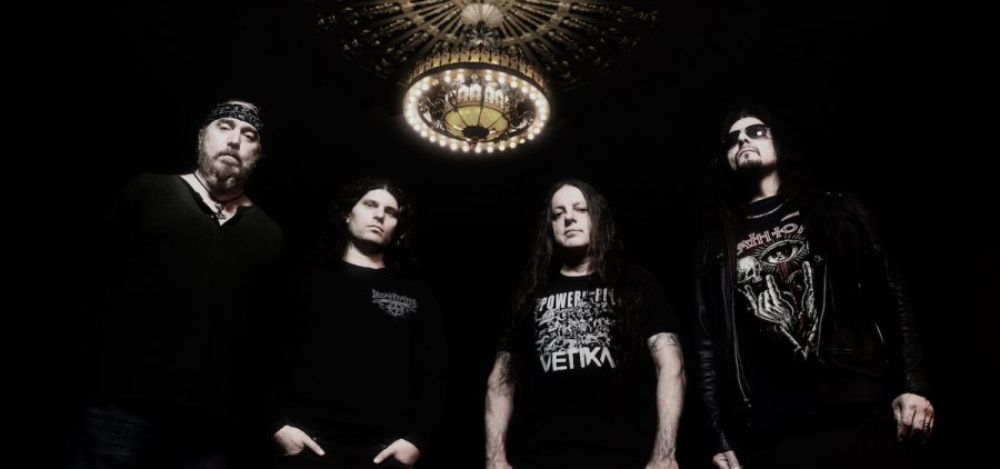 A promotional picture of the band Death To All. There are four members and they are standing together under a chandelier.