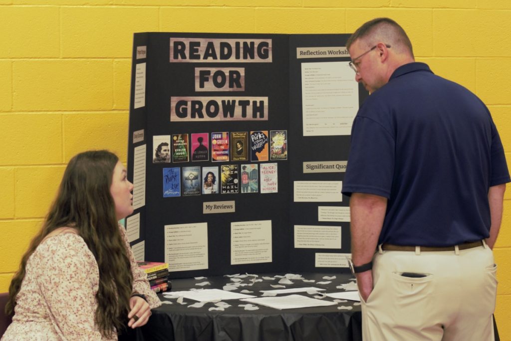 A high school student presents a poster about reading to her school's superintendent.