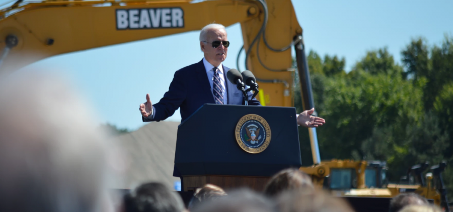 President Joe Biden stands in front of a construction crane giving a speech.
