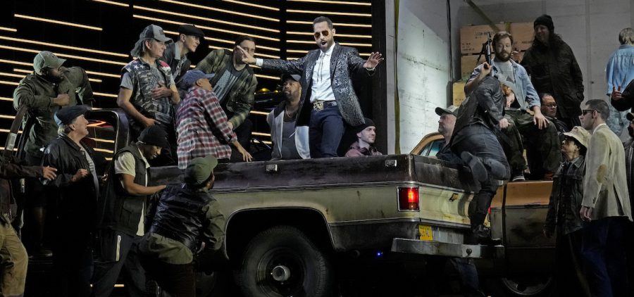 Kyle Ketelsen as Escamillo in Bizet's "Carmen." He's singing in the back of an old pickup truck surrounded by a crowd of people CreditKen Howard / Met Opera