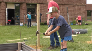 A child is hammering a metal rod into the corner of a garden bed at Trimble Elementary and Middle School using a hammer.