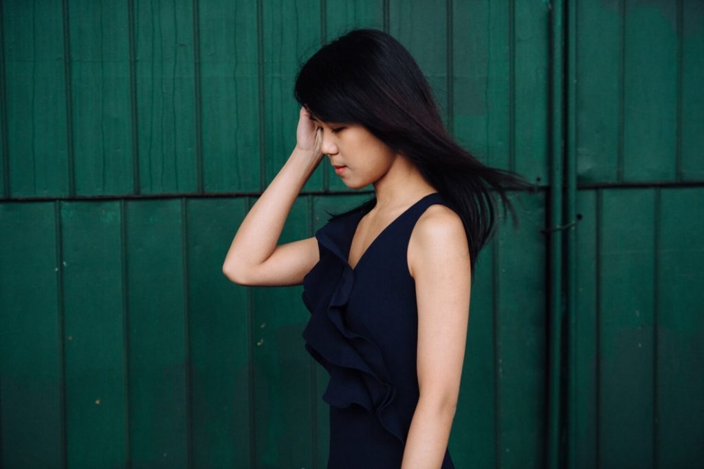 A promotional image of pianist Kate Liu. She is wearing a black dress and is posed in front of a green wall.