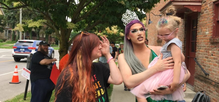 A drag queen holds a child while another woman stands close by.
