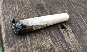 A marijuana joint with a burnt end sits on a wooden table.