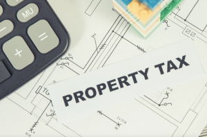 A calculator and some lego blocks sit on a pile of papers with the word "PROPERTY TAX" printed on large letters.