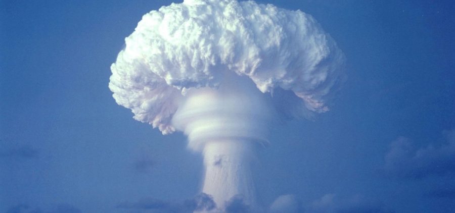 massive white mushroom cloud after a large bomb explosion shown in contract to clear blue sky