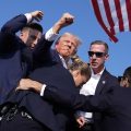 Former president Trump thrust his fist in the air as he is surrounded by Secret Service and with blood on his face.