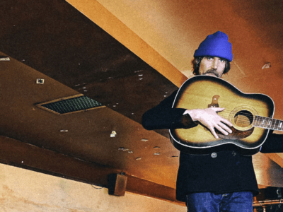 An image of Dean with his guitar and a blue beanie.