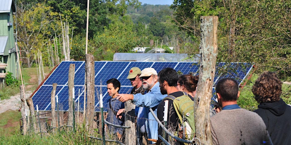 A group of people gathered by a solar energy panel outside.