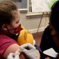 A person in a mask puts a band-aid on a child's arm.