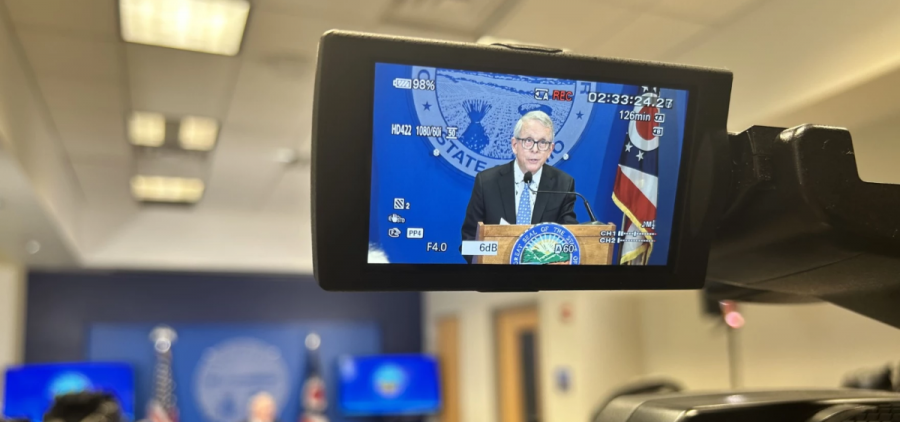 An image of Governor Mike DeWine appears on the view screen of a TV camera during a press conference.