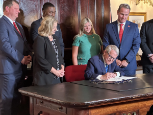 Ohio Governor Mike DeWine signs a bill into law while other people stand behind him.