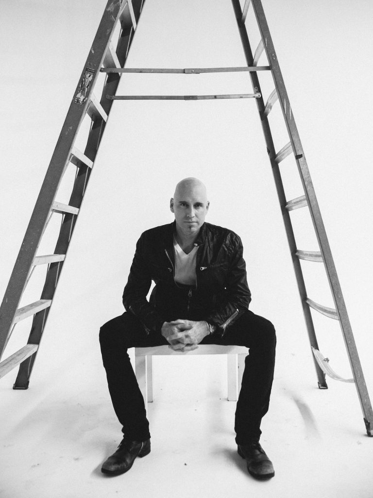 Matt Scannell sits under a ladder for a black and white promotional photo. 