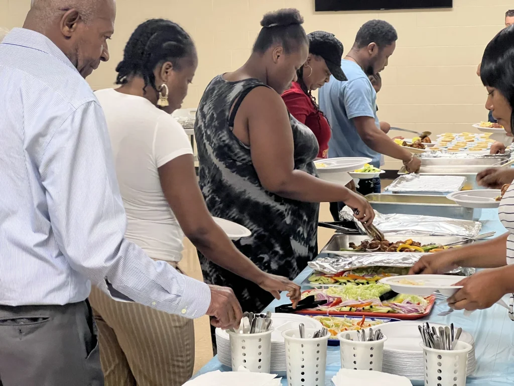 People serve traditional Haitian food, cooked by local Haitian residents, to people in line at the "Lunch and Learn" session