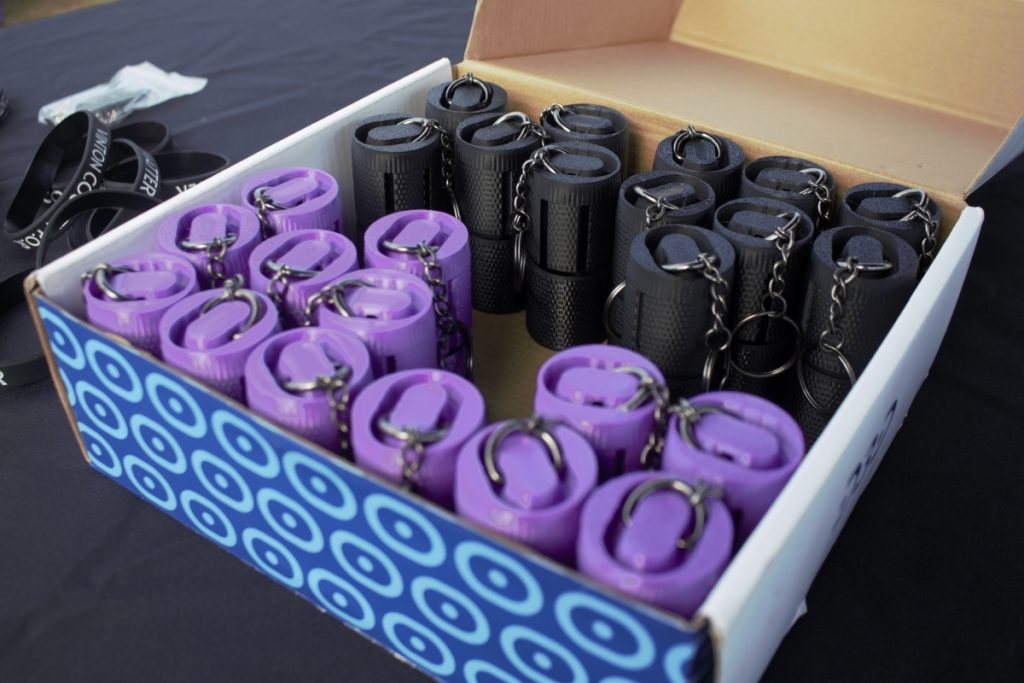 A box with cylindrical 3D-printed purple and black capsules that can attach to a keychain.