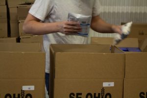 A volunteer places bags of food into cardboard boxes on an assembly line.