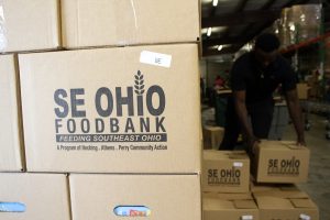 Boxes with "SE OHIO FOODBANK" written on them are stacked high as a volunteer stacks more in the background.