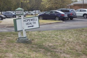 A white sign with green borders reads "HOPEWELL HEALTH" with an arrow pointing to a parking lot.