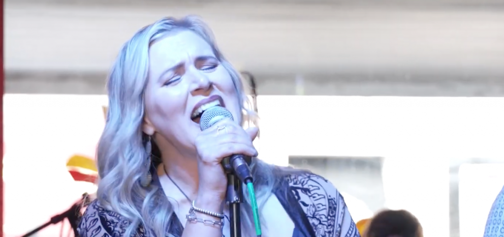 An image of a woman with long blonde hair singing into a microphone.