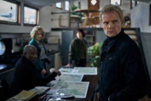 Piet Van der Valk (Marc Warren) looking towards door, with three others in the room