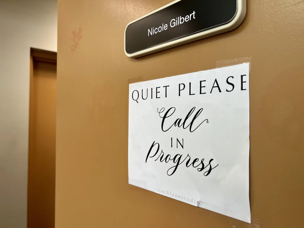 A sign on Nicole Gilbert's door reads "Quiet Please. Call in Progress"