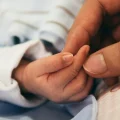 A woman's hand holds a newborn baby's hand.