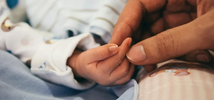 A woman's hand holds a newborn baby's hand.