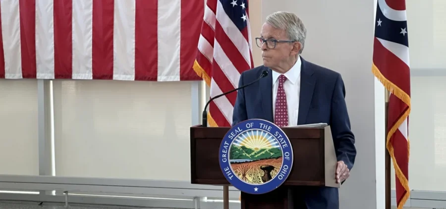 Gov. Mike DeWine takes a question at a press conference from behind a podium.