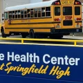 Busses pull up to the front of a school with a sign in front of them highlighting the Health Center at Springfield High