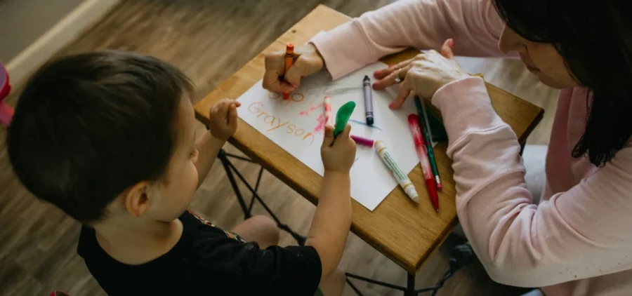 A woman and a child draw in crayon on a piece of paper together