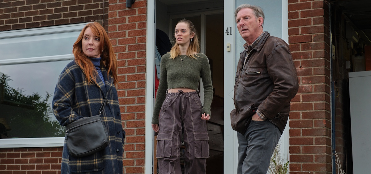 Three characters, two with hands in pockets, standing in front of brick home looking at someone - or something in front of them