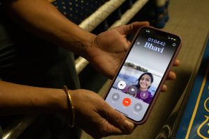 A pair of hands hold a smartphone in the middle of a call. There is a photo of a girl and the name "Bhavi."