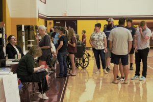 A group of high school students and parents father in a school gymnasium to look at a number of student presentations.