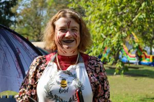 A woman with fake blood on her face and an apron poses outside.