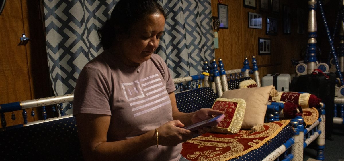 A woman sits on a couch in a dark living room with a phone in her hand.