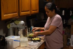 A woman standing at a kitchen counter, putting pasta into a plastic container.