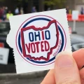 A hand holds up an Ohio voted sticker