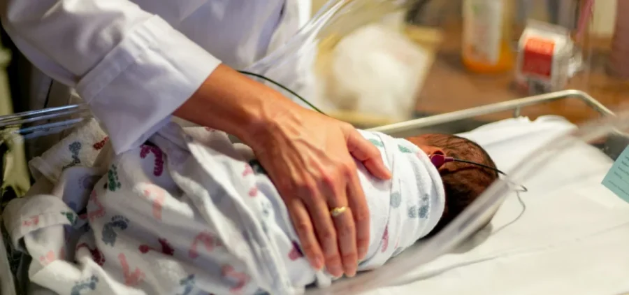 A person comforts a baby in a hospital crib