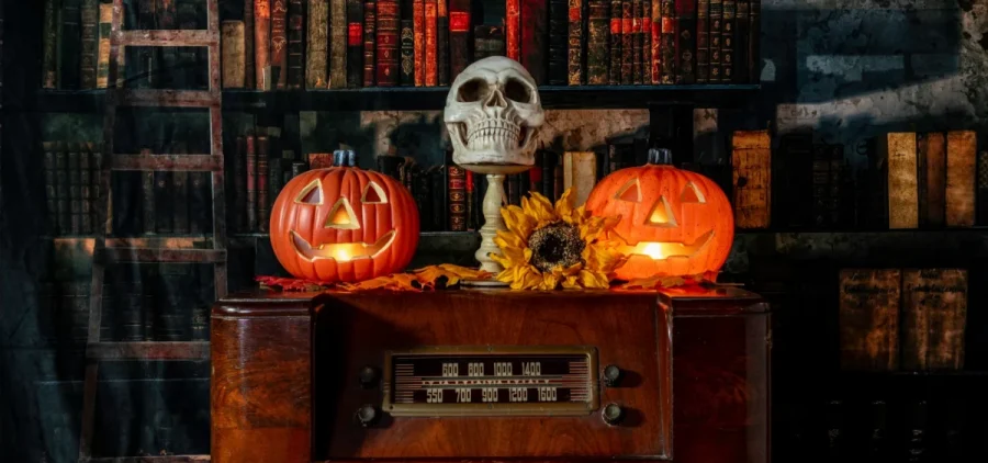 A scary picture has two jackolanterns and a skull on top of an old radio.