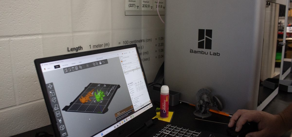 A laptop shows a design in the computer program CAD. It is next to a 3D printer.