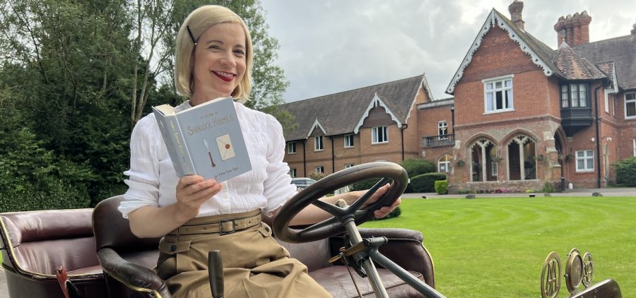 Lucy Worsley in vintage car holding The Return of Sherlock Holmes at Audleyswood Hotel, Hampshire. Credit: Lorian Reed-Drake © BBC Studios