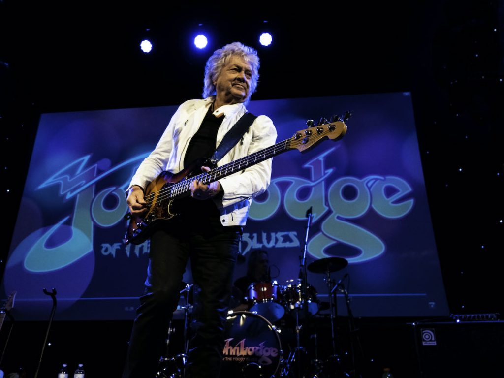 An image of John Lodge playing on stage. 